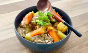 Un délicieux tajine agneau aux carottes et pommes de terre, garni de coriandre fraîche. Une cuillère en bois repose sur le plat.