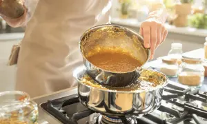 Une personne verse un liquide doré, du caramel à sec, d'une casserole à une autre sur une cuisinière.