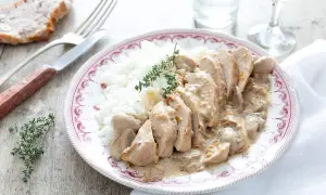 Une assiette de riz blanc avec des tranches de poulet nappées d'une sauce onctueuse au poulet crème champignon, garnie de thym frais.