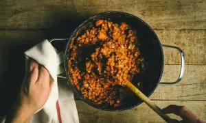 Cuisson lente de lentilles vertes dans une cocotte, avec une cuillère en bois et une main tenant un torchon.