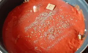Sauce tomate maison mijote dans une poêle, agrémentée d'herbes et d'un cube de bouillon.