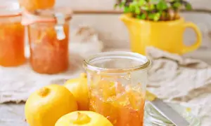 Bocaux de marmelade de citron italienne, avec des citrons frais et une plante verte dans un pichet jaune en arrière-plan.