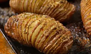 Pommes de terre nouvelles coupées en accordéon, dorées et garnies d'herbes et de fromage, prêtes à être dégustées.