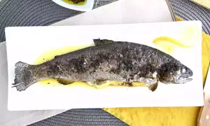 Une truite au four entière, dorée et savoureuse, servie sur une assiette blanche avec des quartiers de citron. Un délice simple et sain.