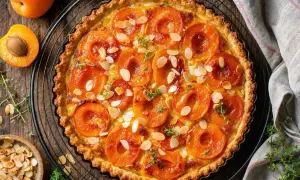 Une délicieuse tarte aux abricots classique, garnie d'amandes effilées et de thym frais, prête à être dégustée.