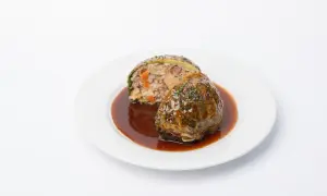 Chou farci, une recette du carnet de Julie, servi avec une sauce brune et garni d'herbes.