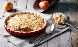Un délicieux crumble pomme tout juste sorti du four, servi dans un plat rouge, avec une portion sur une cuillère ornée.