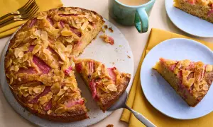 Un délicieux dessert rhubarbe gastronomique, un gâteau aux amandes effilées et à la rhubarbe rose, servi sur une assiette bleue.