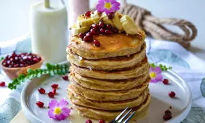 Pile de pancake banane, garnie de fruits rouges, de rondelles de banane et de fleurs roses. Un délice pour le petit-déjeuner.