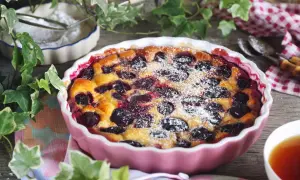 Un délicieux clafoutis aux prunes, saupoudré de sucre glace, prêt à être dégusté avec une tasse de thé.