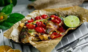 Dorade en papillote, savoureuse et colorée, garnie de tomates cerises, d'olives et d'une tranche de citron vert.
