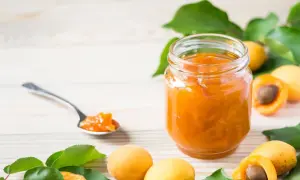 Un pot de confiture abricot peu sucrée, avec des abricots frais et une cuillère remplie de cette délicieuse confiture.