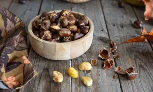 Châtaignes dorées et craquelées, fraîchement sorties de l'air fryer, dans un bol en bois. Quelques châtaignes décortiquées et leurs coquilles éparpillées sur la table en bois.