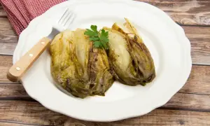 Deux endives fondue à la poêle, garnies de persil, sur une assiette blanche avec une fourchette.