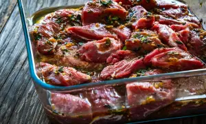 Morceaux de joue de porc marinés dans un plat en verre, prêts pour une délicieuse recette.