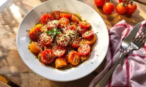 Tomates à la provençale à la poêle, garnies de parmesan râpé et de basilic frais, sur une assiette blanche.
