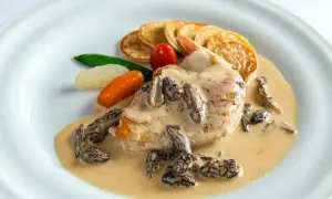 Un plat de poulet en sauce crémeuse avec des morilles, des mini-crêpes, des carottes et des petits pois. Le jus de poulet est riche et onctueux.