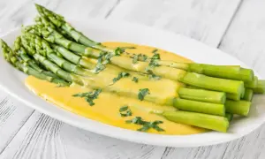 Asperges vertes fraîches nappées d'une sauce onctueuse et dorée, parsemées d'herbes. Un délice de sauce pour asperges chaudes.