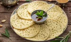 Une assiette de crêpes mille trous, garnie d'une coupelle de miel et de menthe fraîche, prête à être dégustée.