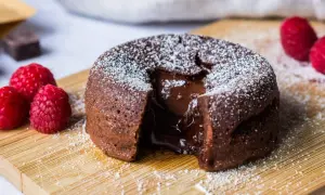 Un fondant au chocolat dégoulinant de cœur coulant, saupoudré de sucre glace, avec des framboises fraîches sur une planche en bois.