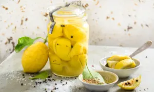 Un bocal de citrons confits au sel, prêts pour une recette citron confit sucre. Des épices et du gros sel parsèment la table.