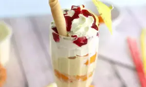 Un déliceux pêche Melba, avec des couches de fruits, de crème fouettée et de coulis de fruits rouges, garni d'une gaufrette et d'un petit parasol.