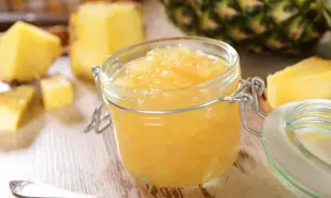 Un pot de confiture d'ananas maison, entouré de morceaux d'ananas frais et d'une cuillère.