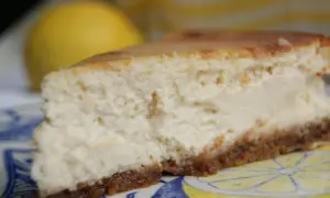 Tranche de cheesecake ricotta citron, crémeuse et légère, sur une assiette décorée de citrons.