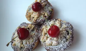 Trois petites tartelettes aux cerises, saupoudrées de sucre glace et ornées d'une cerise fraîche sur le dessus.
