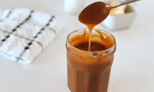 Une cuillère verse un caramel beurre salé onctueux dans un pot en verre.