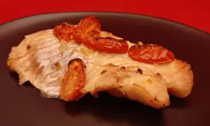 Un délicieux filet de dorade au four, garni de tomates cerises rôties, sur une assiette noire.