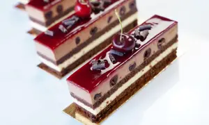 Délicieux entremets Forêt Noire, une symphonie chocolatée et cerise, parsemée de copeaux de chocolat et surmontée d'une cerise fraîche.