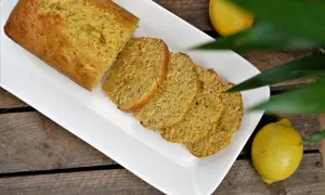 Un délicieux cake citron pavot, coupé en tranches, servi sur une assiette blanche, avec des citrons frais à côté.