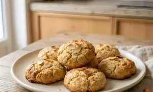 Une assiette de meilleurs biscuits aux amandes, dorés et garnis de lamelles d'amandes, sur une table en bois.