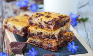 Gourmandises de cake banane pépite chocolat, empilées sur une ardoise, décorées de fleurs bleues et de morceaux de chocolat noir.