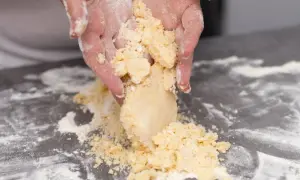 Mains travaillées, saupoudrées de farine, façonnant une pâte sablée friable sur un plan de travail.