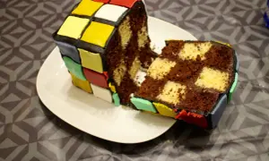 Un gâteau Rubik's cube, coupé en deux, révèle un intérieur marbré chocolat et vanille. Les couleurs vives du glaçage rappellent le célèbre casse-tête.