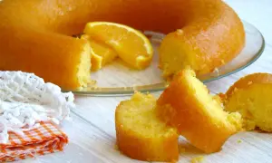 Un délicieux cake à l'orange, avec des tranches d'orange fraîche, servi sur une assiette en verre. Une part est déjà coupée.