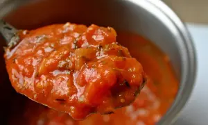 Une cuillère débordante de tomate concassée, parfumée d'herbes, prête à garnir un plat.