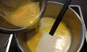 Préparation d'une recette crémeux vanille Michalak : on verse un mélange d'œufs battus dans une casserole contenant du lait et une spatule.