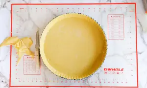 Pâte brisée salée prête à être garnie dans un moule à tarte. Des chutes de pâte et un couteau sont à côté.