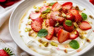 Délicieuse salade de fruits maison : fraises fraîches, pistaches croquantes et menthe fraîche sur une crème onctueuse, arrosée de miel.