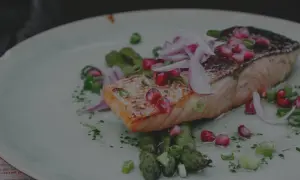 Un délicieux saumon air fryer, garni de grenade et d'oignon rouge, servi avec des asperges vertes.