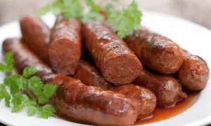 Assiette de merguez au four, dorées et juteuses, garnie de persil frais. Un délice prêt à être dégusté.