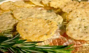 Délicieuses tuiles parmesan poêle, croustillantes et dorées, parsemées d'herbes. Une branche de romarin frais ajoute une touche aromatique.