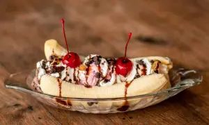 Un déliceux banana split garni de crème fouettée, de cerises et de sauce au chocolat, prêt à être dégusté.