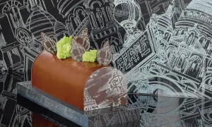 Bûche de Noël chocolatée, décorée de chocolat blanc et de mousse verte, évoquant une recette Pierre Hermé. Le fond présente des croquis architecturaux parisiens.