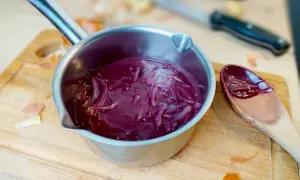 Sauce porto facile mijotant dans une casserole, avec des oignons rouges et une cuillère en bois.