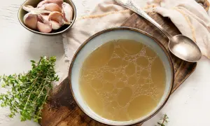 Un bol de bouillon de volaille doré, avec de l'ail et du thym. Idéal pour savoir comment faire un bouillon de volaille savoureux.
