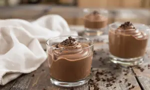 Trois verrines de mousse au chocolat Alain Ducasse, garnies de copeaux de chocolat, sur une table en bois rustique.